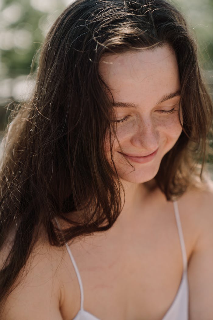 A smiling woman with long hair enjoying a sunny day outdoors.